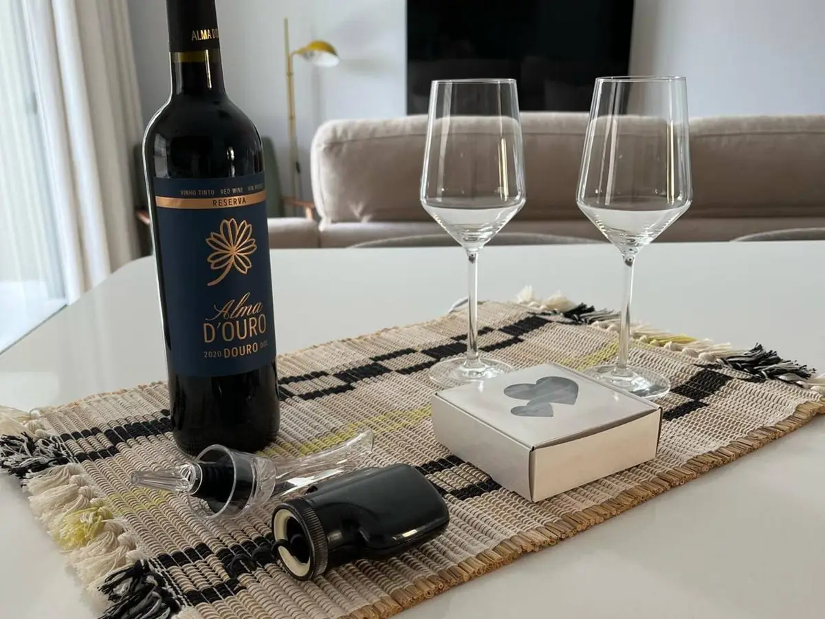 Garrafa de vinho, dois copos e uma caixa de boas-vindas na mesa da sala